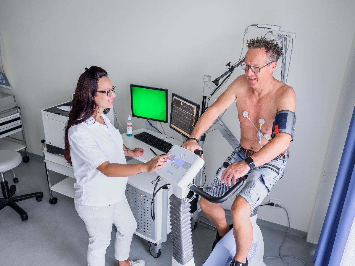Ein Mann auf dem Ergometer und eine Therapeutin daneben