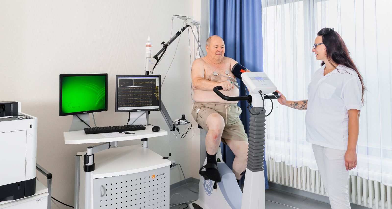 Ein Mann auf dem Ergometer und eine Therapeutin daneben