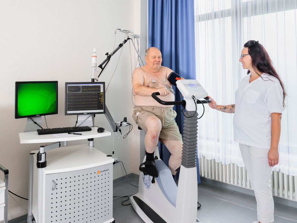 Ein Mann auf dem Ergometer und eine Therapeutin daneben